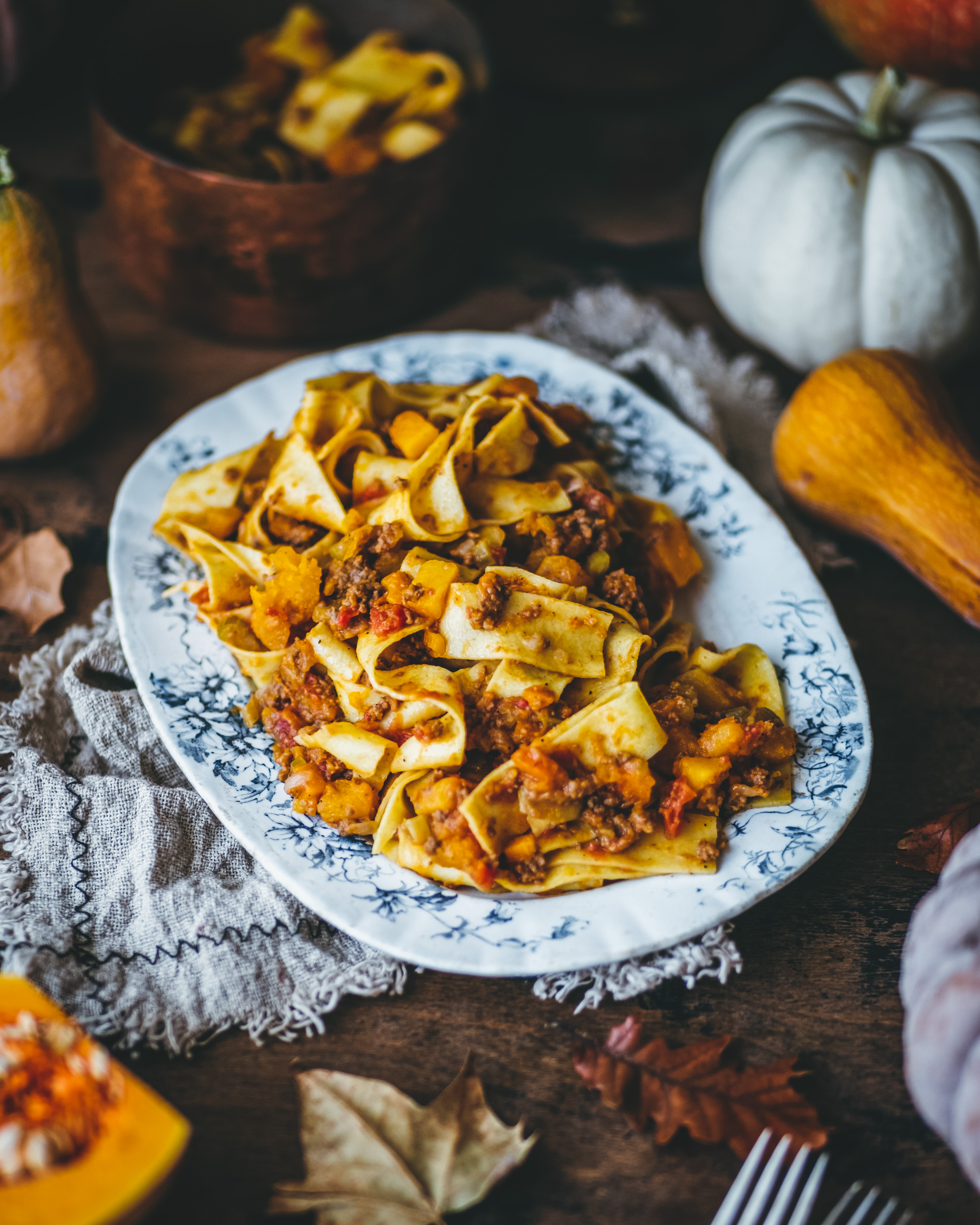 A serving platter filled with papardelle pasta, coated in beef bolognese with butternut squash.