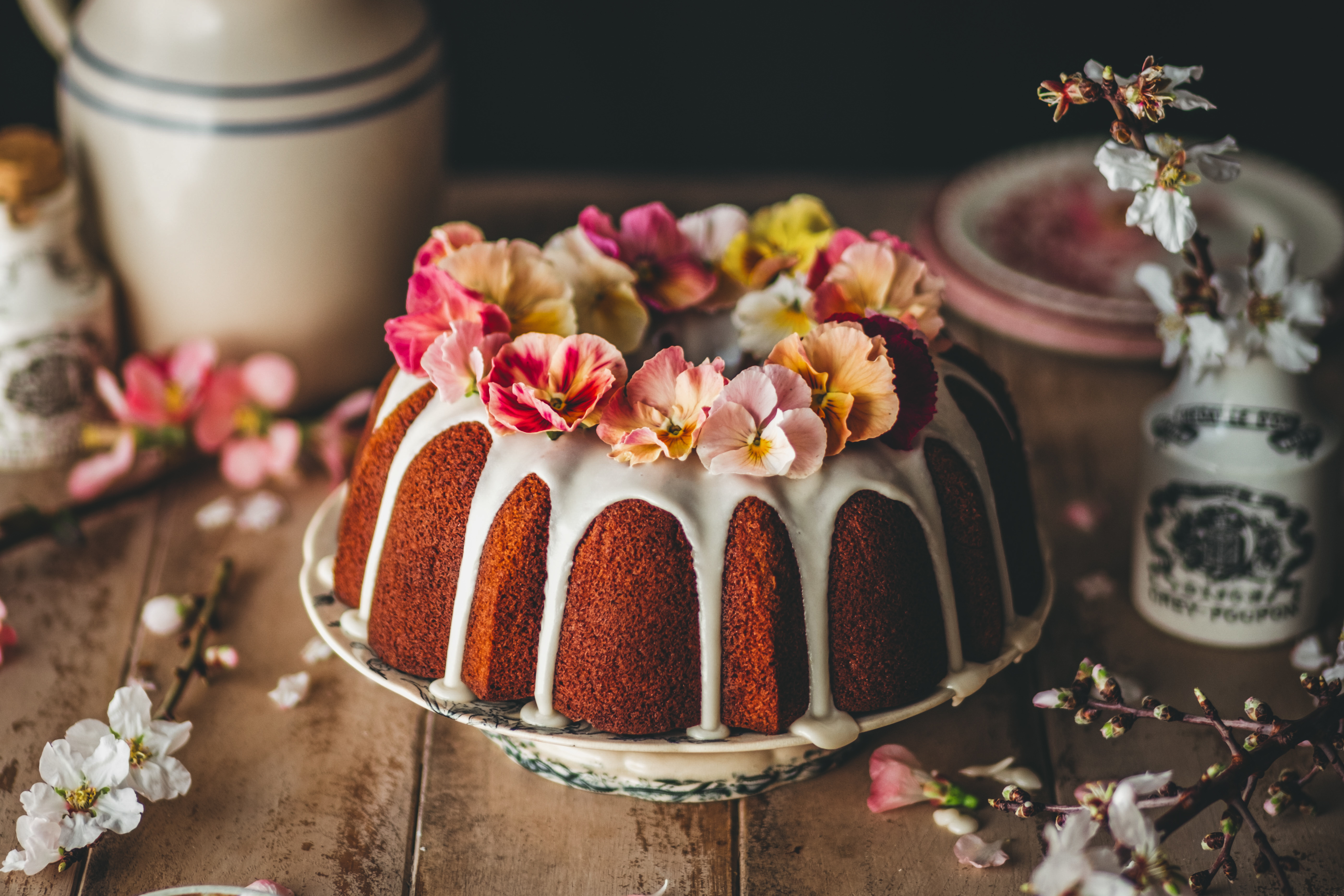 a bundt cake decorated with warm-toned pansies, surrounded by almond blossoms