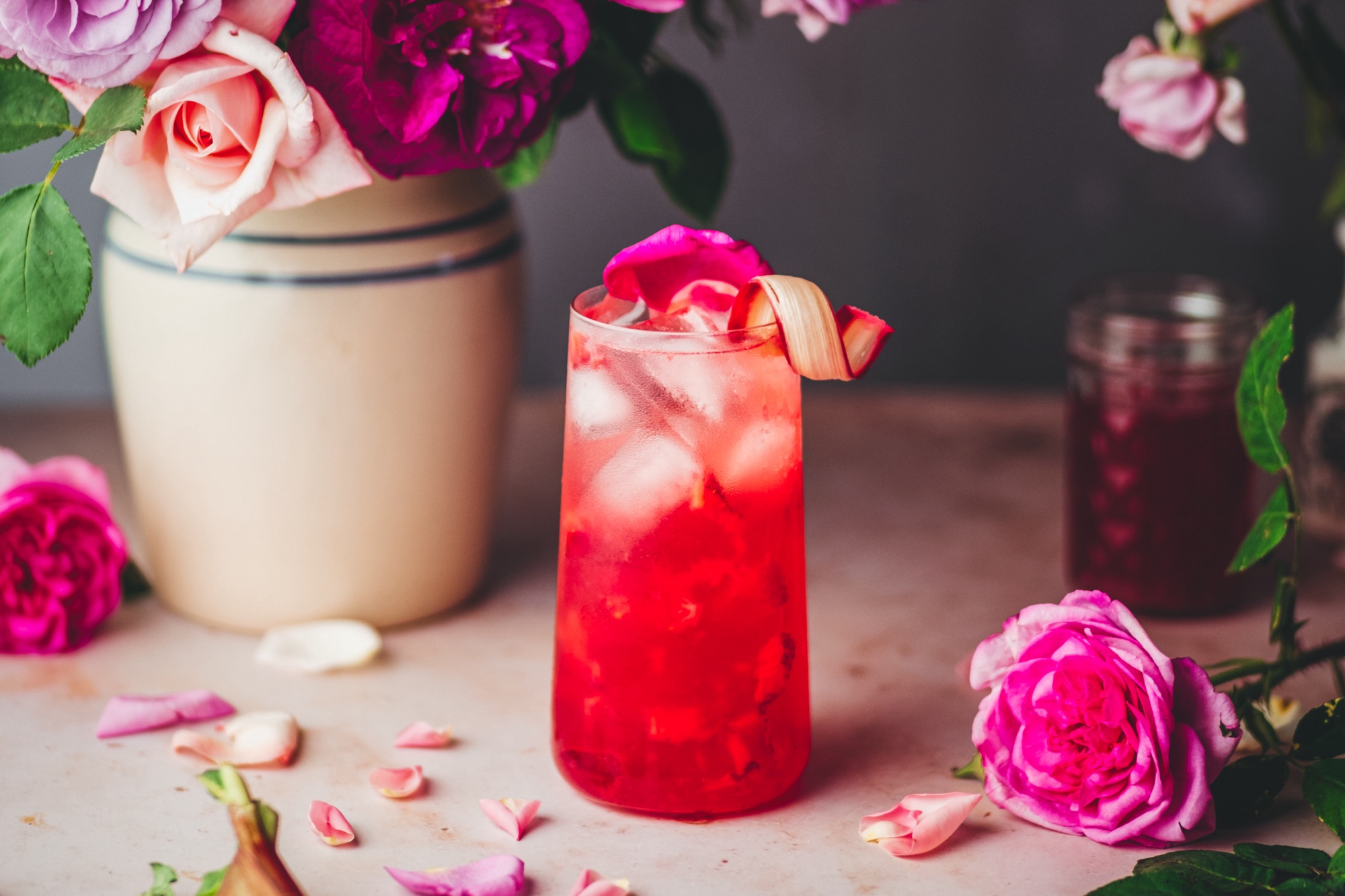 Bright pink Empress Elderflower Rose Gin cocktail styled with rosepetals and rhubarb.