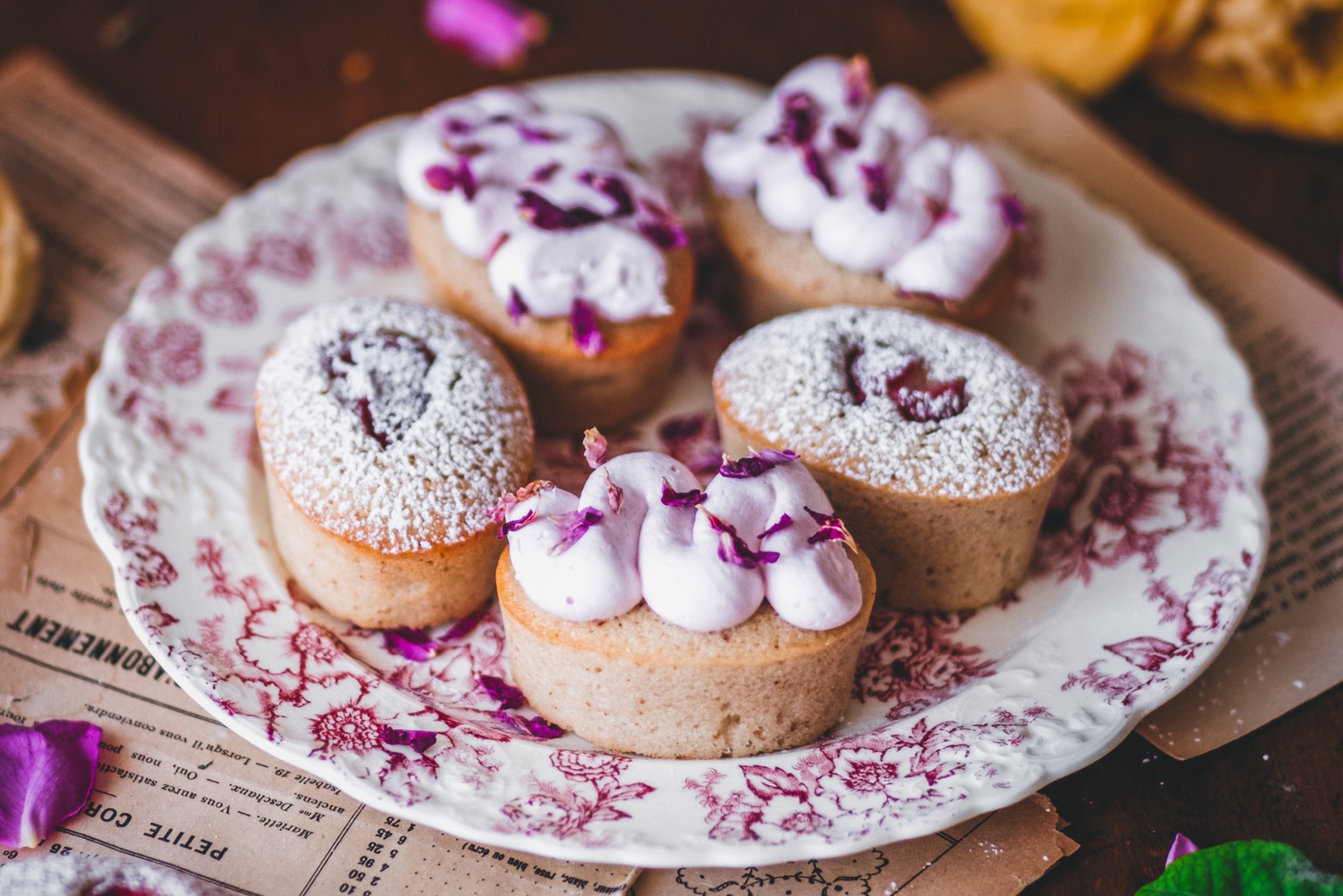 Financiers topped with rhubarb and rose buttercream, styled on a pink vintage plate with rose petals surrounding.